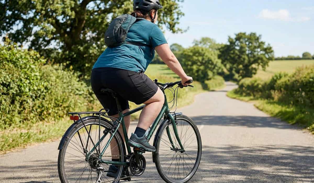 Frau mit kräftigen Oberschenkeln fährt Fahrrad auf Landstraße – Radfahren mit Lipödem in großen Größen