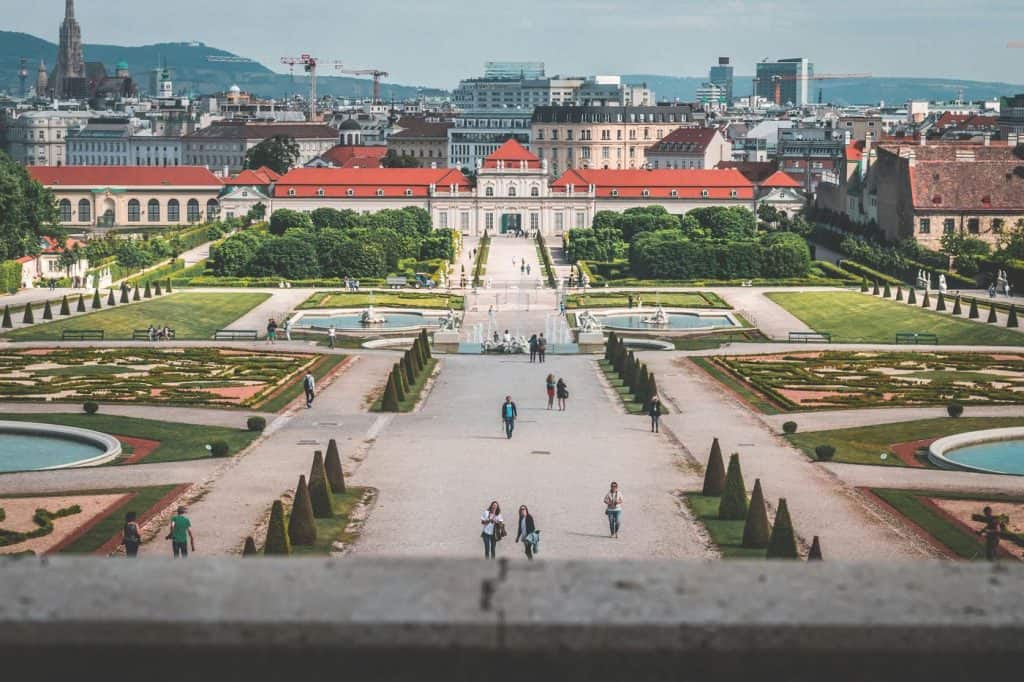 Blick auf einen formellen Garten mit Wegen, Brunnen und Stadt im Hintergrund.