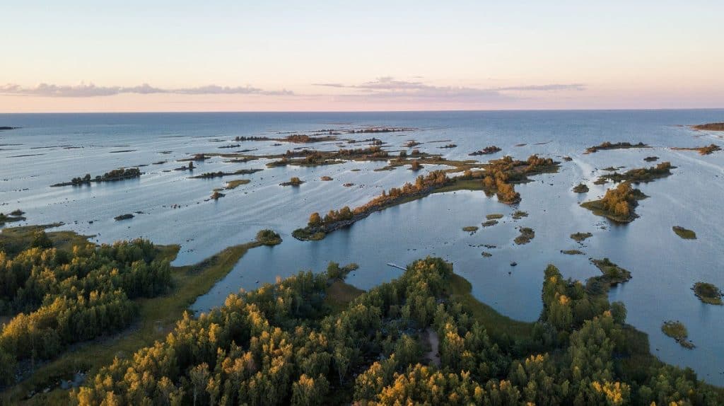 Aerial view of a coastal archipelago with tree-covered islands and narrow waterways at sunset.