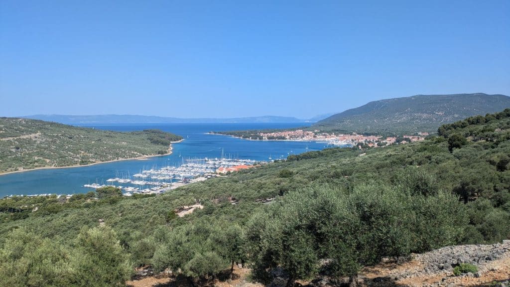 Blick auf eine Bucht mit Yachten, umgeben von Hügeln und Bergen bei klarem Himmel.