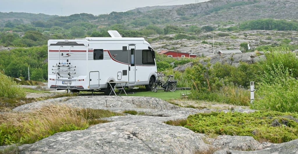 Wohnmobil auf Campingplatz mit Fahrrad und Natur im Hintergrund.