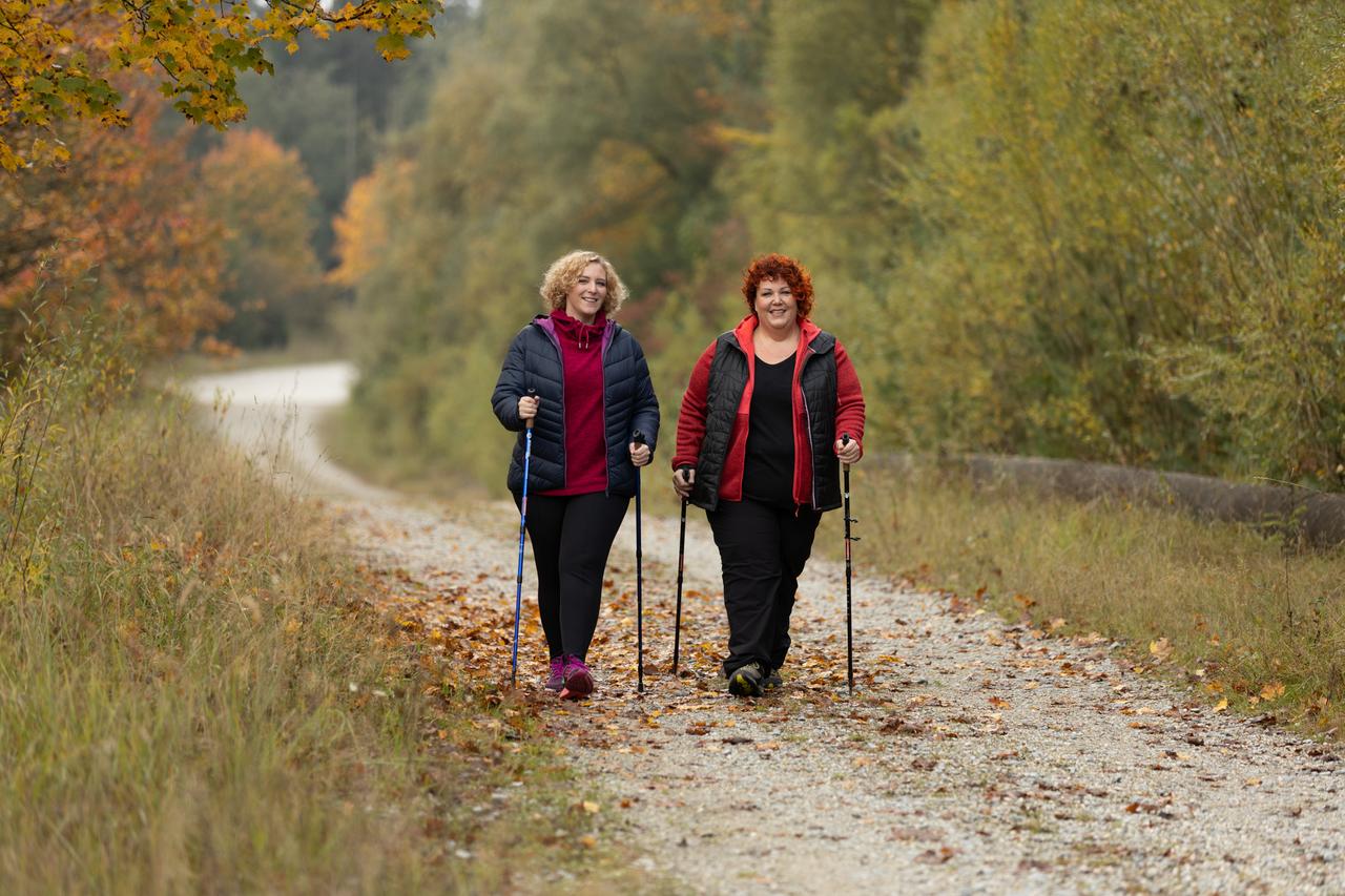 Zwei Frauen beim Nordic Walking auf einem Herbstweg in dunklen Outdoorhosen, der Saum endet über dem Schuh