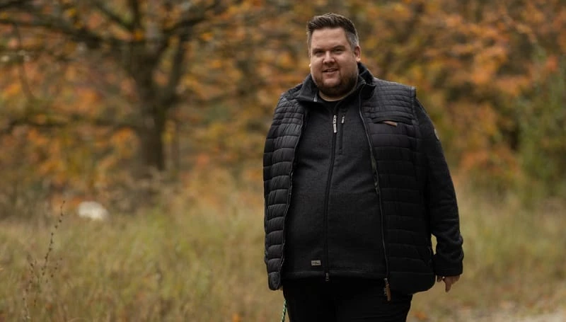 Herren Outdoorbekleidung in Uebergroessen: Steppweste ueber Fleecejacke im Herbstwald
