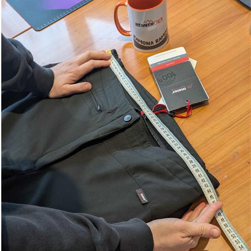 Ramona misst eine Outdoorhose flach aus Ramona misst eine Outdoorhose von Maier Sports flach liegend mit dem Maßband aus